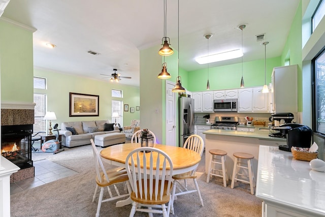 carpeted dining area featuring ceiling fan, crown molding, and a tiled fireplace