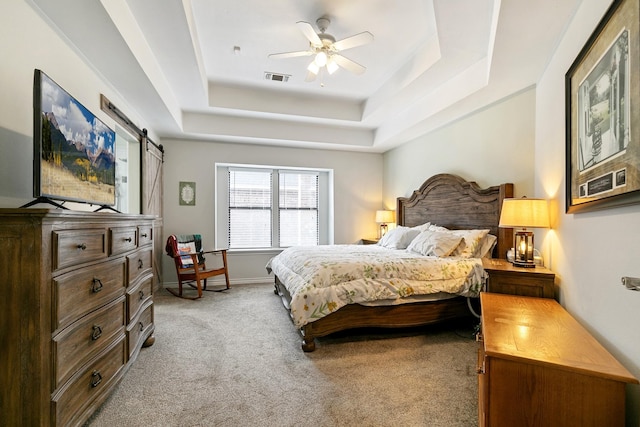 bedroom with a raised ceiling, a barn door, ceiling fan, and light carpet