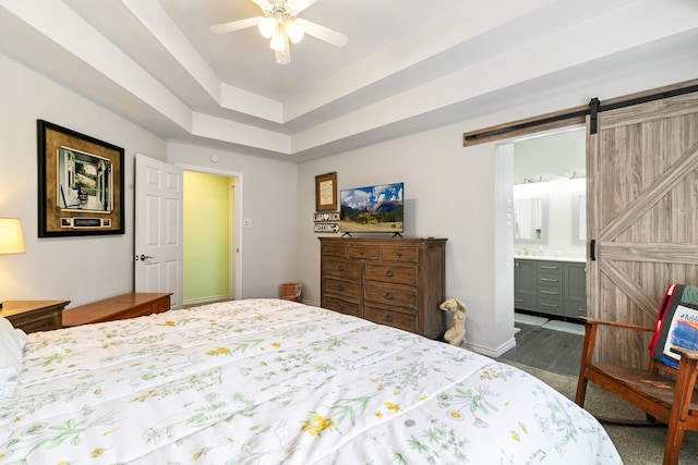 bedroom with connected bathroom, a barn door, ceiling fan, and a tray ceiling