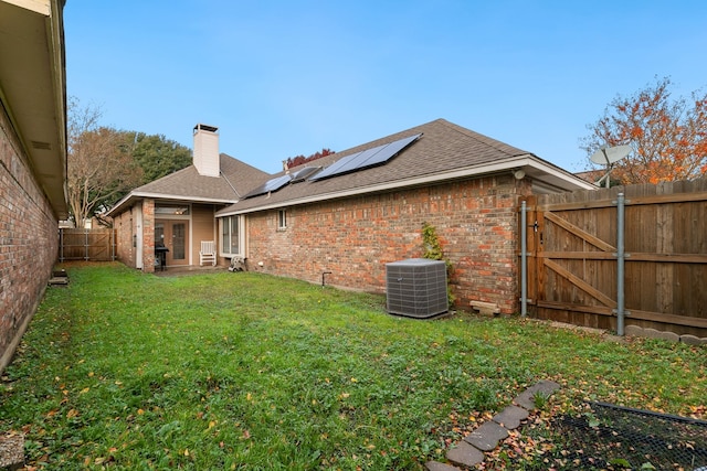 back of house with a yard, central AC unit, and solar panels