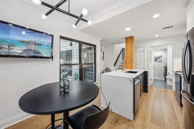 kitchen featuring washer / dryer, stainless steel appliances, sink, light hardwood / wood-style flooring, and crown molding