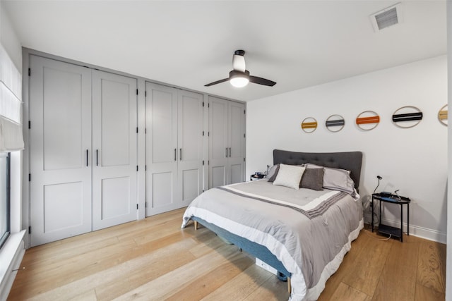 bedroom featuring ceiling fan, light hardwood / wood-style flooring, and multiple closets