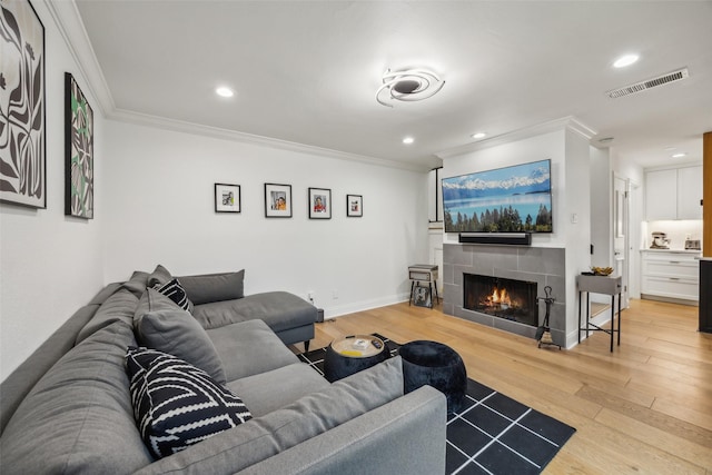 living room featuring hardwood / wood-style floors, crown molding, and a tiled fireplace