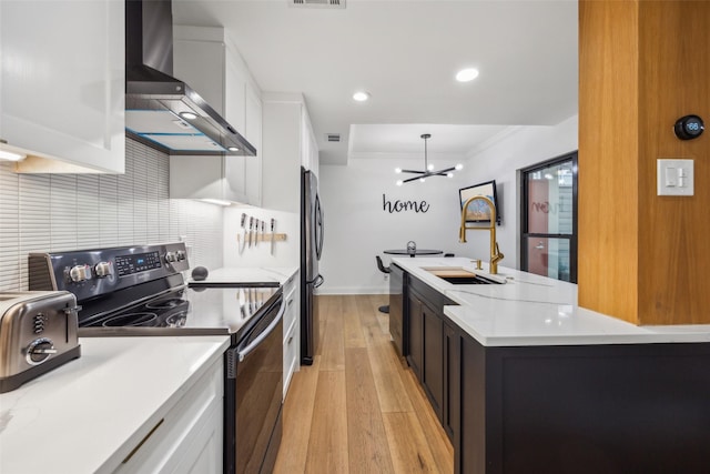 kitchen with wall chimney exhaust hood, white cabinetry, stainless steel appliances, sink, and a chandelier