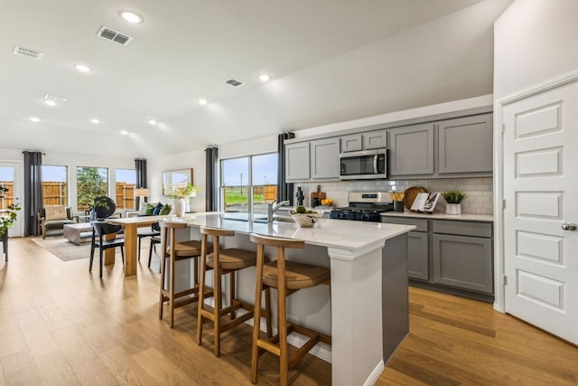 kitchen with a kitchen bar, gray cabinetry, a kitchen island with sink, and stainless steel appliances