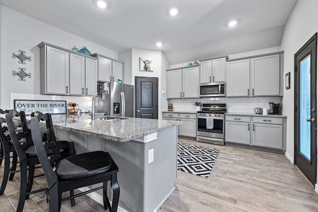 kitchen with gray cabinetry, light stone countertops, stainless steel appliances, backsplash, and kitchen peninsula