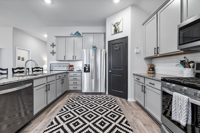 kitchen with tasteful backsplash, gray cabinetry, light stone countertops, and appliances with stainless steel finishes