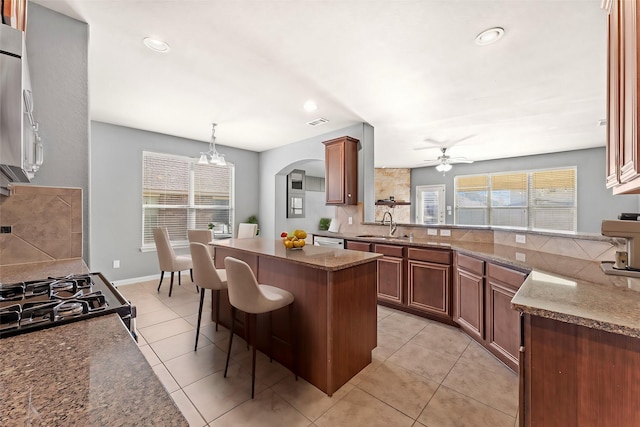 kitchen featuring sink, hanging light fixtures, a breakfast bar area, light tile patterned flooring, and ceiling fan with notable chandelier