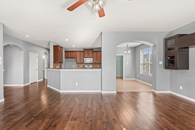 unfurnished living room featuring ceiling fan with notable chandelier and dark hardwood / wood-style flooring