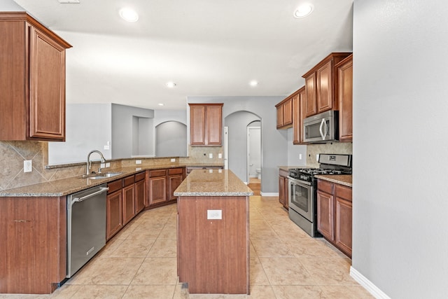 kitchen with light stone countertops, kitchen peninsula, stainless steel appliances, sink, and a kitchen island