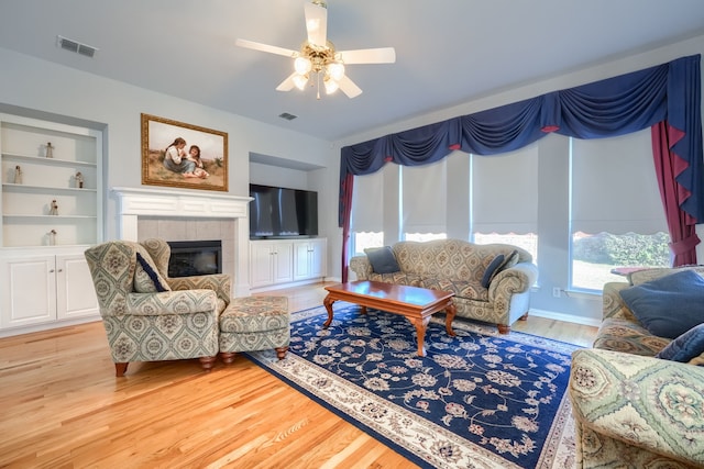 living room featuring ceiling fan, built in features, a healthy amount of sunlight, and light hardwood / wood-style flooring