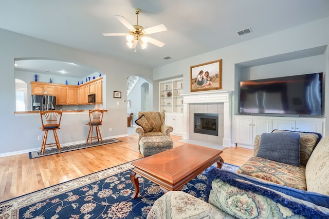 living room with a fireplace, ceiling fan, built in features, and light hardwood / wood-style flooring