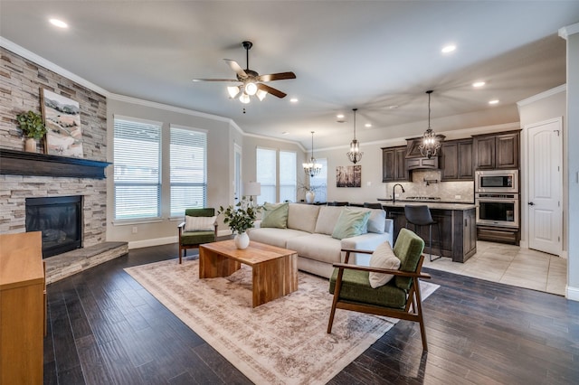 living room with crown molding, ceiling fan with notable chandelier, hardwood / wood-style floors, and a fireplace