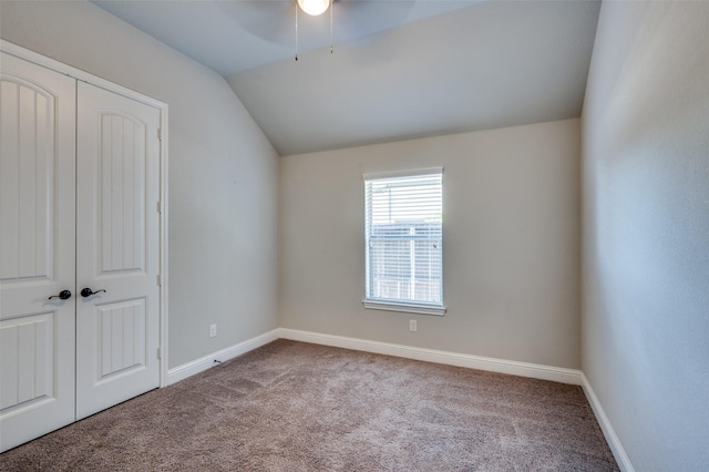 unfurnished bedroom featuring a closet, ceiling fan, carpet, baseboards, and lofted ceiling