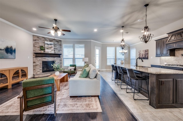 living room featuring baseboards, ornamental molding, light wood-style floors, a fireplace, and ceiling fan with notable chandelier