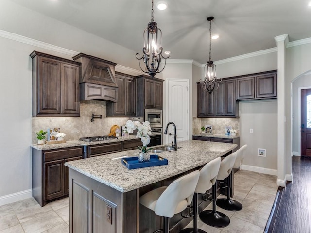 kitchen featuring dark brown cabinets, decorative backsplash, stainless steel appliances, premium range hood, and light stone countertops