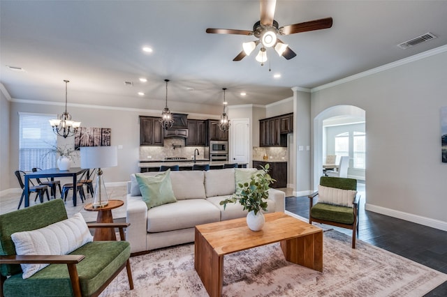 living area featuring arched walkways, wood finished floors, visible vents, baseboards, and ornamental molding