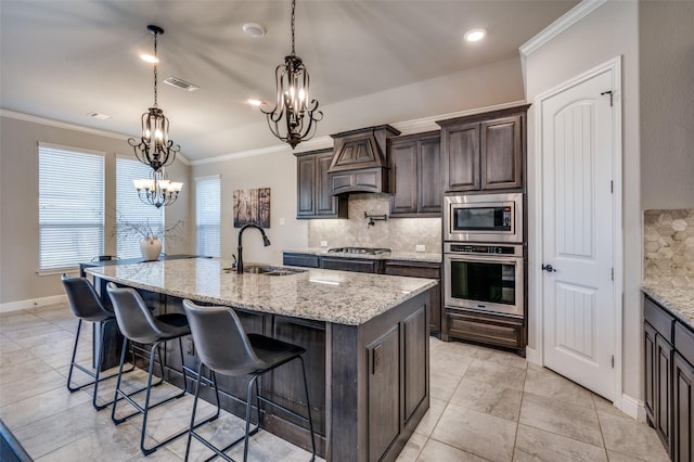 kitchen featuring an island with sink, appliances with stainless steel finishes, custom exhaust hood, crown molding, and a sink