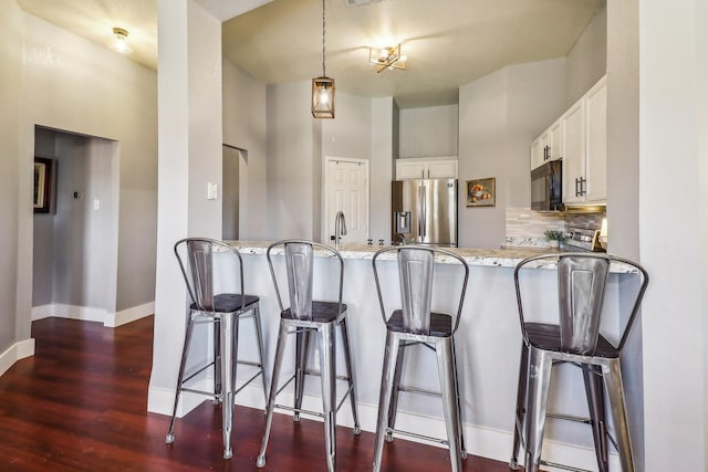 kitchen featuring kitchen peninsula, stainless steel fridge with ice dispenser, light stone countertops, white cabinetry, and a breakfast bar area