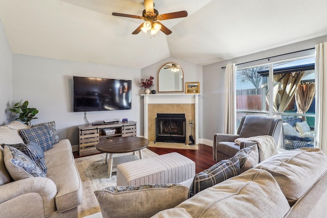 living room with ceiling fan, lofted ceiling, a tiled fireplace, and wood-type flooring