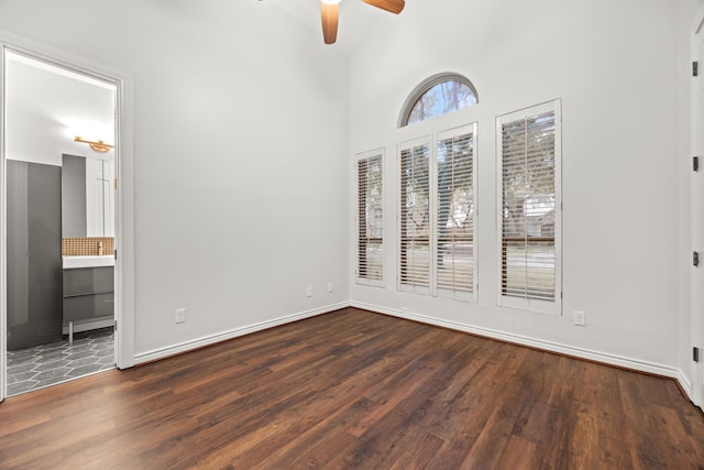 empty room featuring ceiling fan, a high ceiling, wood finished floors, and baseboards