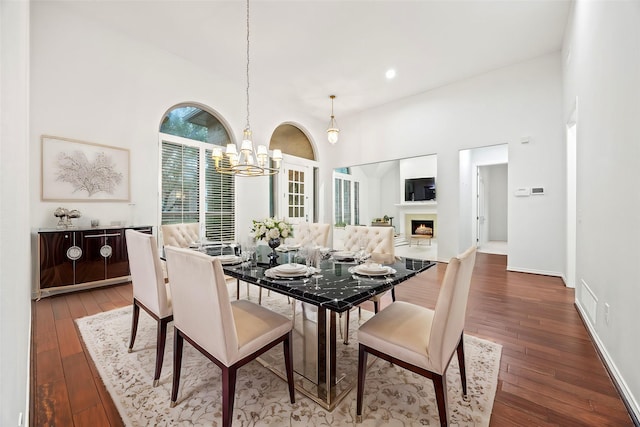 dining area featuring a warm lit fireplace, visible vents, wood-type flooring, a high ceiling, and a notable chandelier