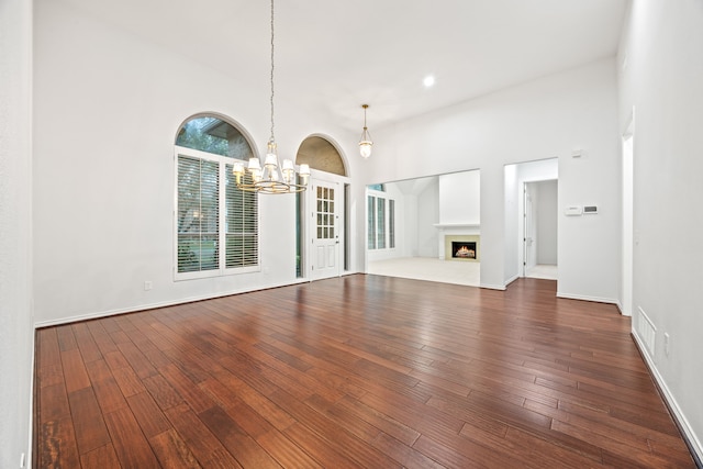 unfurnished living room with recessed lighting, dark wood-style flooring, baseboards, a lit fireplace, and an inviting chandelier