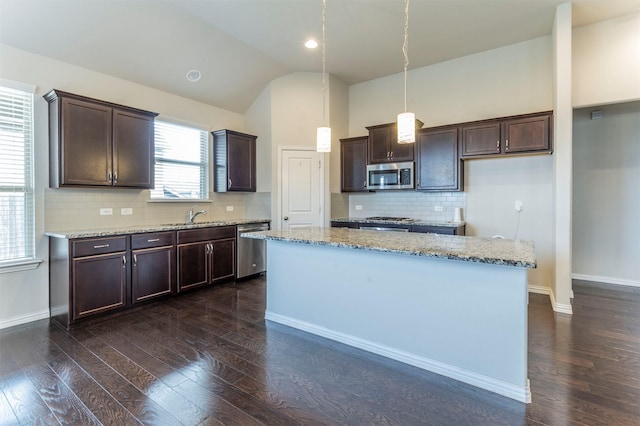 kitchen featuring stainless steel appliances, light stone counters, pendant lighting, vaulted ceiling, and a kitchen island