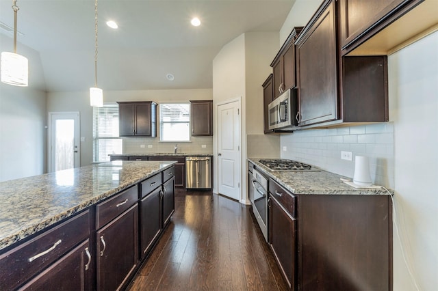 kitchen featuring pendant lighting, backsplash, dark brown cabinets, light stone counters, and stainless steel appliances