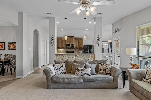 living room featuring a towering ceiling, light colored carpet, and ceiling fan