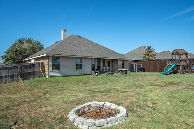 back of property featuring a fire pit, a lawn, and a playground