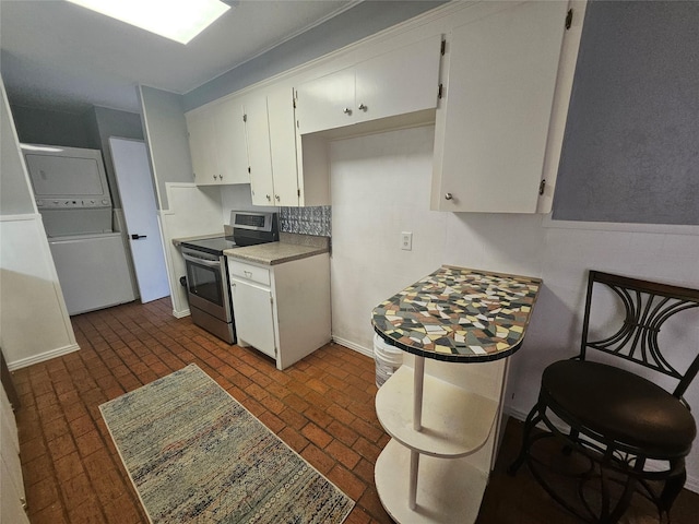 kitchen featuring white cabinetry, stacked washer / drying machine, and stainless steel electric stove