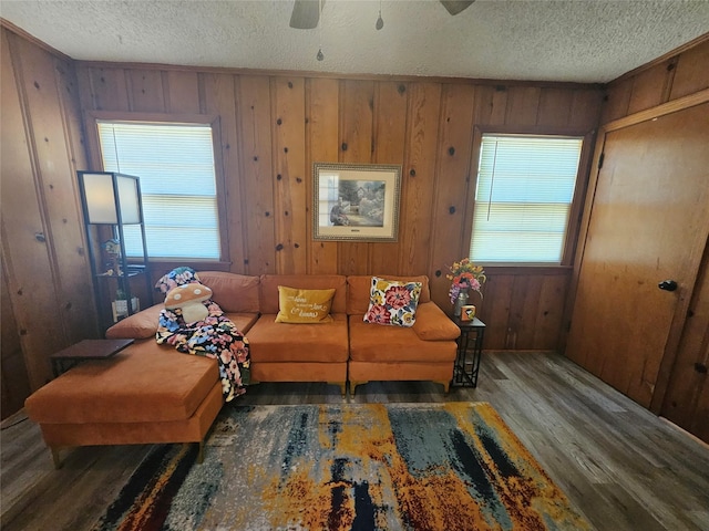 living room with dark hardwood / wood-style flooring, a textured ceiling, wooden walls, and ceiling fan