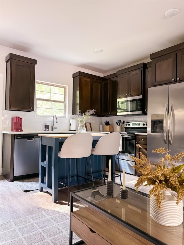 kitchen featuring sink, stainless steel appliances, light hardwood / wood-style flooring, a breakfast bar, and dark brown cabinets