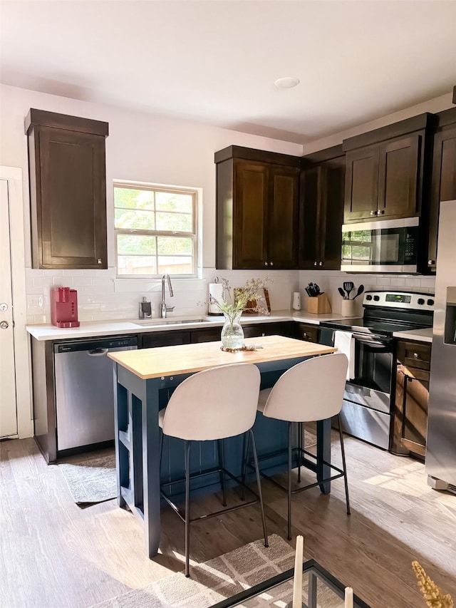 kitchen with appliances with stainless steel finishes, sink, a kitchen bar, a center island, and dark brown cabinets