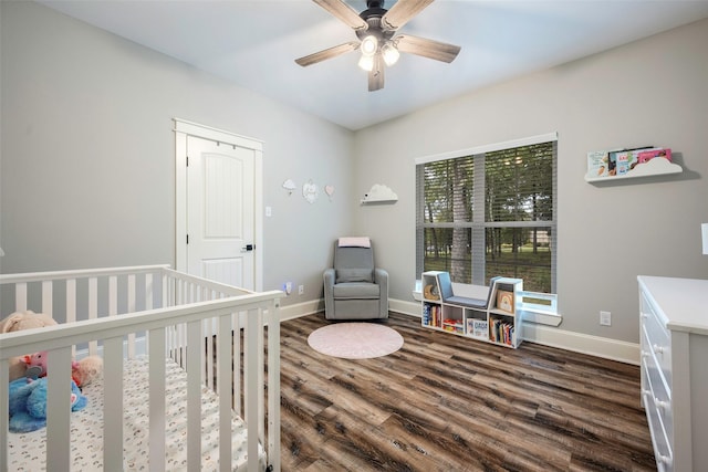 bedroom featuring a nursery area, dark wood-type flooring, and ceiling fan