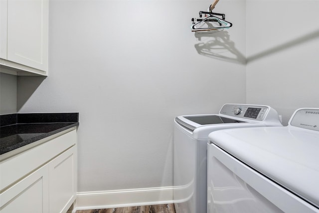 clothes washing area featuring dark hardwood / wood-style floors, washing machine and dryer, and cabinets