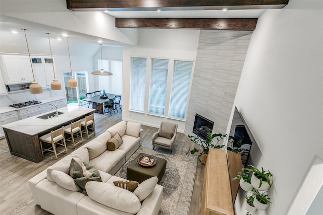 living room featuring beamed ceiling, light wood-type flooring, sink, and a tile fireplace