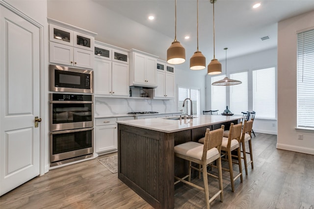 kitchen featuring built in microwave, sink, a center island with sink, white cabinetry, and hanging light fixtures