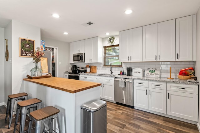 kitchen with a breakfast bar, white cabinets, sink, appliances with stainless steel finishes, and dark hardwood / wood-style flooring