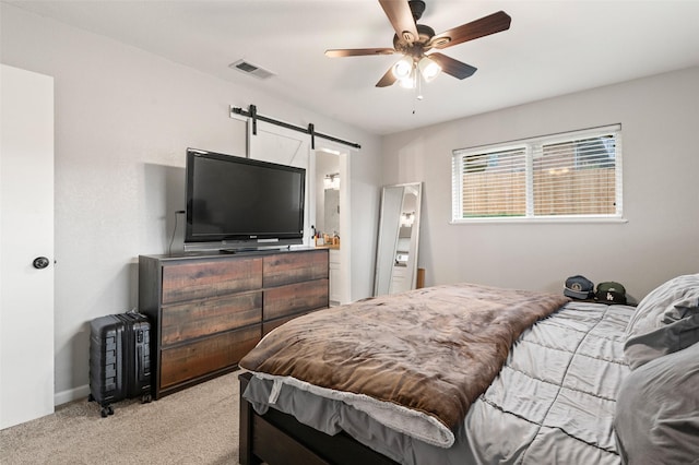 bedroom with a barn door, light colored carpet, ceiling fan, and connected bathroom