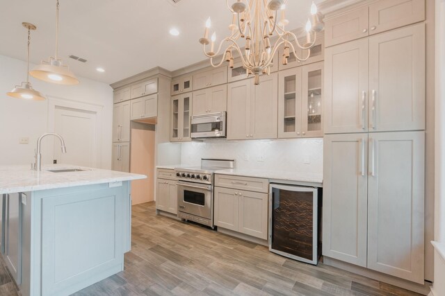 kitchen with light stone counters, stainless steel appliances, beverage cooler, sink, and pendant lighting