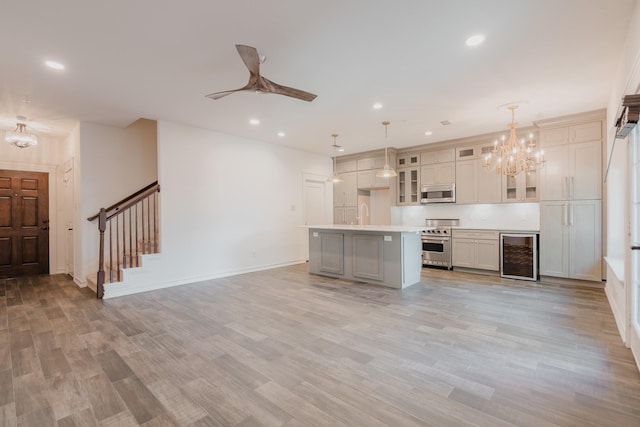 kitchen featuring ceiling fan with notable chandelier, stainless steel appliances, beverage cooler, a kitchen island, and hanging light fixtures