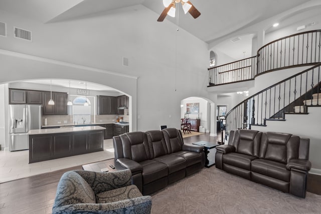 living room with sink, ceiling fan with notable chandelier, high vaulted ceiling, and light hardwood / wood-style flooring