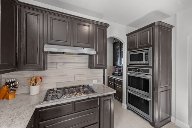 kitchen with dark brown cabinetry, backsplash, light stone counters, and stainless steel appliances