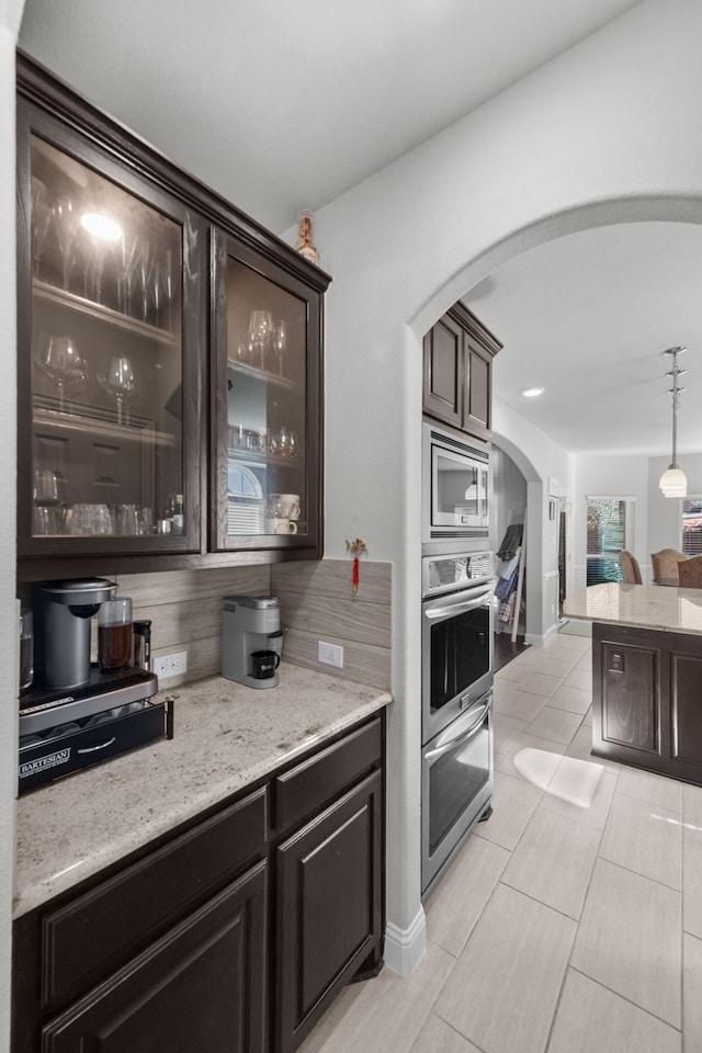 bar featuring light stone counters, stainless steel appliances, decorative light fixtures, and dark brown cabinets