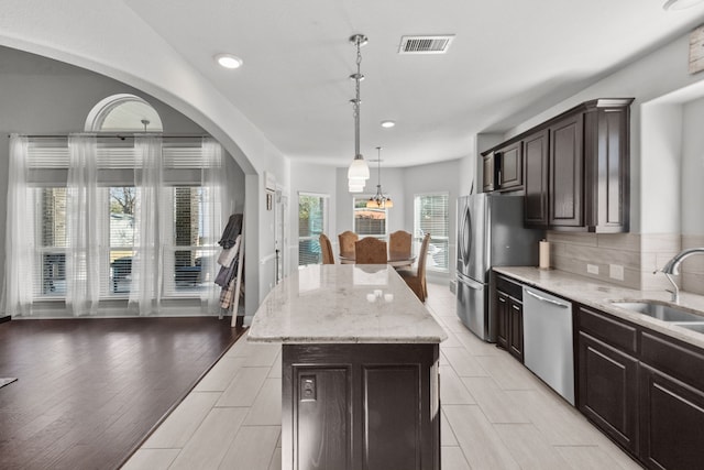 kitchen featuring dark brown cabinetry, sink, decorative light fixtures, a center island, and appliances with stainless steel finishes