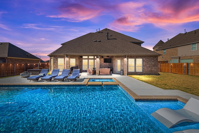 pool at dusk featuring a patio and a lawn