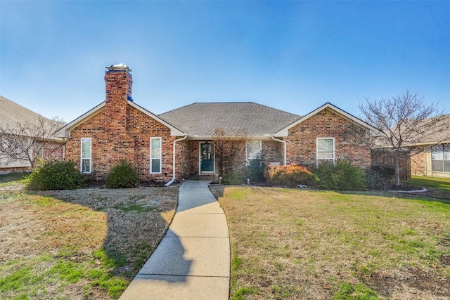 ranch-style house featuring brick siding, a chimney, a front yard, and roof with shingles