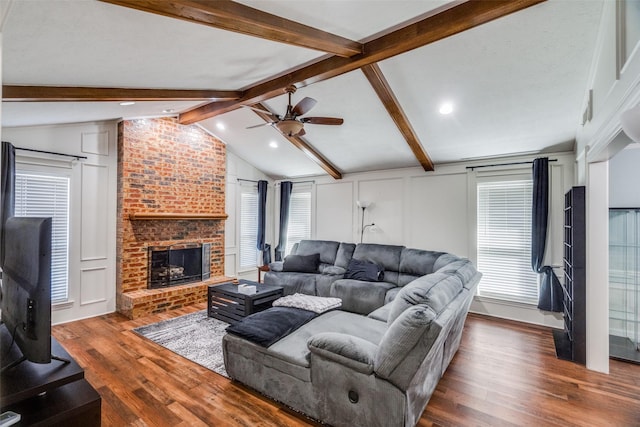 living room with dark wood-type flooring, ceiling fan, a fireplace, and lofted ceiling with beams